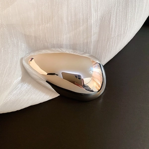 Close-up of pebble-shaped silver brooch with polished mirror finish on white fabric