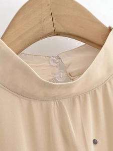Détail de l'encolure du chemisier en mousseline beige avec col officier et boutons clairs