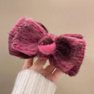Close-up of a plush knitted bow hair clip in pink and purple gradient for winter