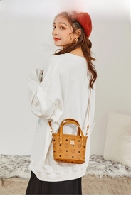 Detail einer braunen Beuteltasche mit Logo-Prints und Goldplakette am weißen Outfit