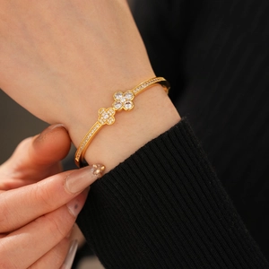 Close-up of golden four-leaf clover clasp bangle with sparkling zircon pavé setting