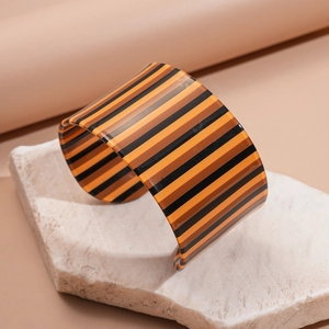 Detail of a wide acrylic C-shaped cuff bracelet with orange and brown stripes on stone