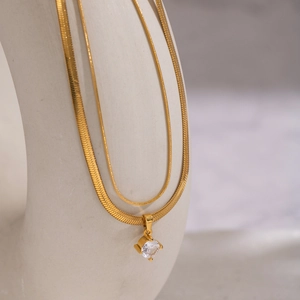 Double-layer gold snake chain necklace with zircon pendant on a beige display stand