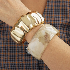 Detail of a wavy gold metal bangle paired with a marbled resin cuff on a suit sleeve