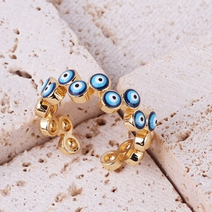 Gold plated evil eye open ring with blue enamel eyes on a natural travertine background