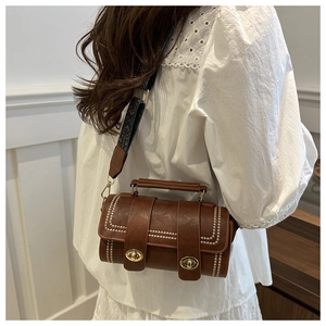 Detail of vintage brown cylinder bag with white stitching and textured wide strap