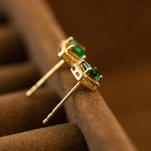 Macro shot of gold square stud earrings featuring sparkling emerald green zircons