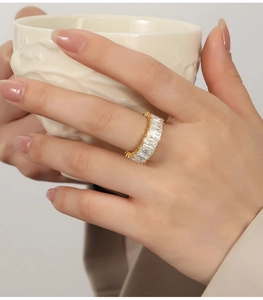 Detail of luxury gold plated ring with rectangular zircons on a hand holding a porcelain cup
