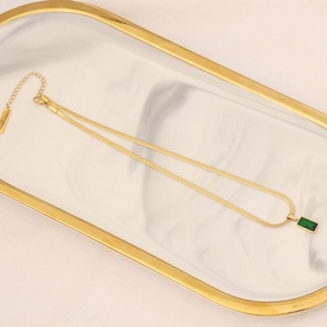 Elegant gold snake chain necklace featuring a green emerald gemstone pendant on marble tray