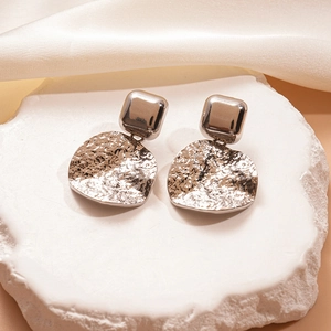 Détail de boucles d'oreilles géométriques en métal argenté avec texture ondulée et clous carrés