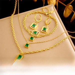 Parure de bijoux dorés avec pierres carrées vert émeraude et détails de double chaîne