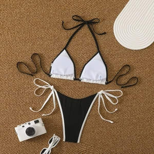 Flat lay of a sexy black and white color-block bikini set on a summer beach straw mat