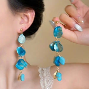 Close-up of long blue shell drop earrings with gold chain link on a model