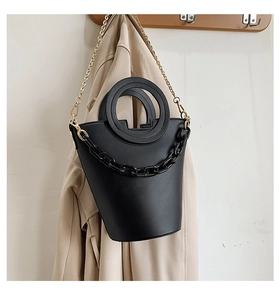 Detail of black bucket bag with dual round handles and stylish thick chain on beige trench