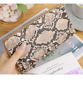 Close-up of snakeskin pattern wallet with gold zipper and wristlet on a wooden table