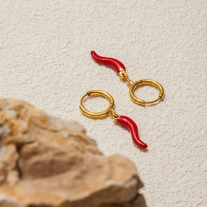 Macro view of gold hoop earrings with red chili pendants on a textured surface