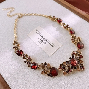 Detail of vintage gold leaf necklace with red faceted gemstone on textured fabric