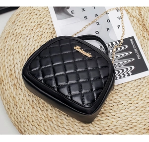 Detail of black quilted leather handbag with gold chain strap and top handle on a beige mat