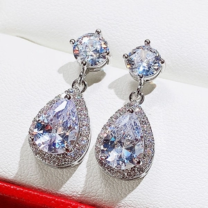 Detailed view of teardrop halo earrings featuring emerald green stones and cubic zirconia