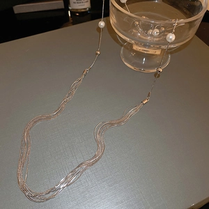 Detail of multi-layer long pearl necklace draped over a glass bowl on grey surface