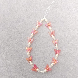 Detailed macro view of beaded phone strap with pink butterfly and white imitation pearls