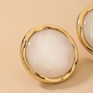 Macro shot of retro round gold-plated earrings with white resin inlay and s925 silver pins