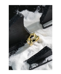 Macro shot of gold wide chain-link hollow ring on textured sand and dark geometric blocks