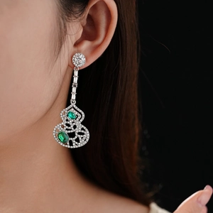 Detail view of hollow wulu drop earrings with green gems on a model's ear