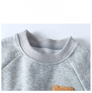 Close-up of grey sweatshirt ribbed crew neck with cute brown fleece bear applique