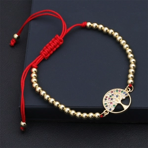 Macro detail of red woven bracelet with gold beads and multi-color tree of life charm