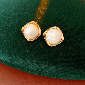 Close-up of gold-plated square studs with elegant white cotton pearls on green velvet