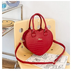 Détail d'un sac à main rouge en forme de cœur avec texture crocodile sur chaise jaune