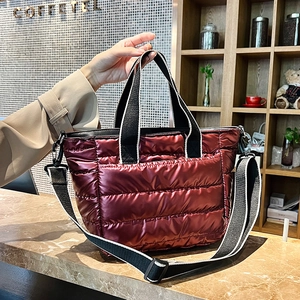 Macro detail of wine red quilted puffy tote bag with glossy finish and striped webbing strap