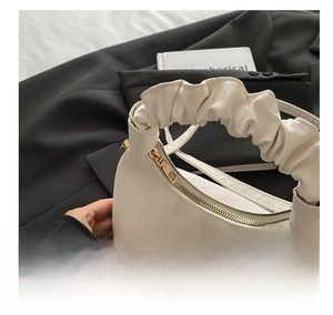 Detail of smooth gold zipper and textured cream leather crescent bag with ruched handle