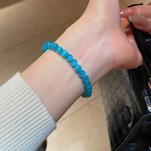 Detailed view of blue cat-eye beaded bracelet worn on wrist against a black leather bag