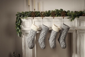 Detail of grey knitted Christmas stockings with cable patterns hanging on white fireplace