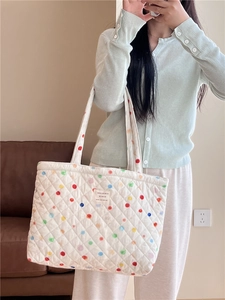 Detailed view of white quilted tote bag featuring vibrant colorful polka dots and patch