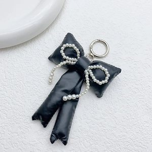 Detail of black puffy bow keychain with pearl chain on white textured surface