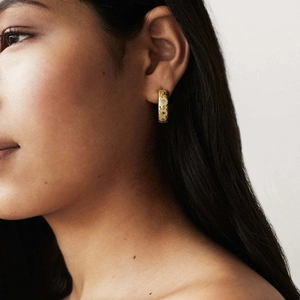 Gold plated C-shaped hoop earrings with white enamel daisy flowers worn by a model