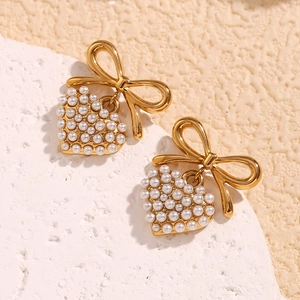 Detail of gold bow earrings with pearl heart pendants on white textured stone background