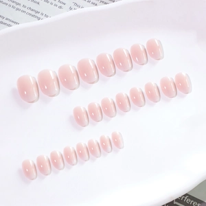 Short round press-on nails with pink white gradient and glossy finish on a white tray