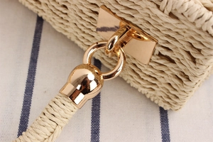 Detail of light gold hardware and straw weaving texture on a square crossbody bag
