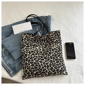 Flat lay of a leopard print canvas tote bag with books and a mobile phone on white linen