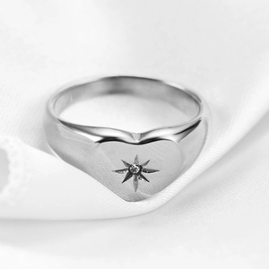 Macro view of silver heart signet ring with engraved star on white silk fabric