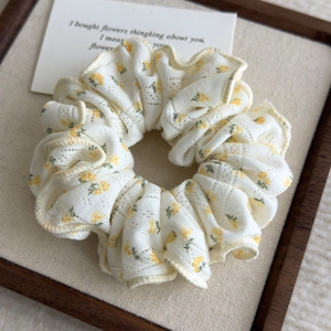 Detail shot of a floral scrunchie in beige fabric with yellow flowers on a wooden tray