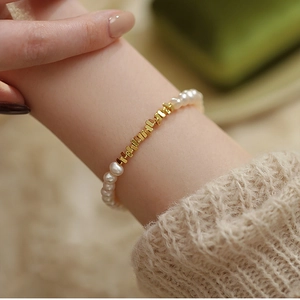 Close-up of a minimalist pearl bracelet with golden metal blocks on a knitted sleeve