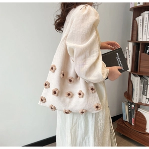 Close-up of cream knitted tote bag featuring brown crochet flowers in a literary setting