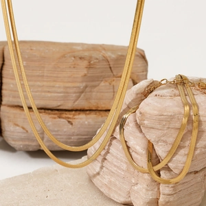 Elegant gold flat snake chain necklace and bracelet set displayed on a natural rock