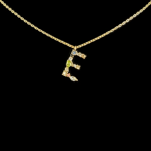 Macro detail of 18k gold letter E pendant with multi-colored gemstones on black background