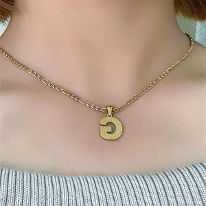Dettaglio di una collana in acciaio inossidabile dorato con ciondolo lettera G e catena